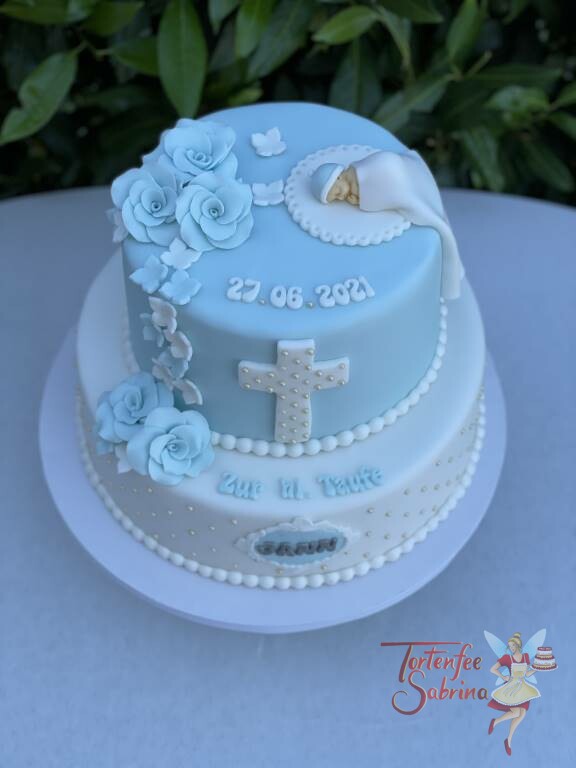 Tauftorte - Kreuz mit Zuckerperlen und süßem Baby unter der weißen Decke, ebenso auf der Torte sind blaue Rosen.