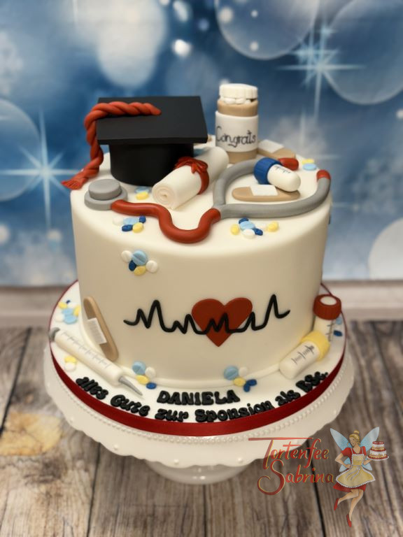 Anlasstorte - Viele Tabletten liegen verstreut auf der Torte. Ganz oben ziert der Diplomhut mit roter Kordel sowie das Stetoskop die Torte.