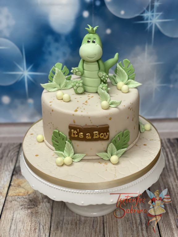 Babytorte - Kleines grünes Dinobaby sitzt oben auf der Torte, umgeben von vielen grünen Blättern und einem Holzschild.