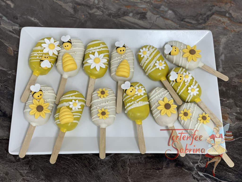 Cakesicles - Bienchen und Blumen zieren die süßen Leckereien, die Schokolade darunter wurde in weiß und gelb gehalten.