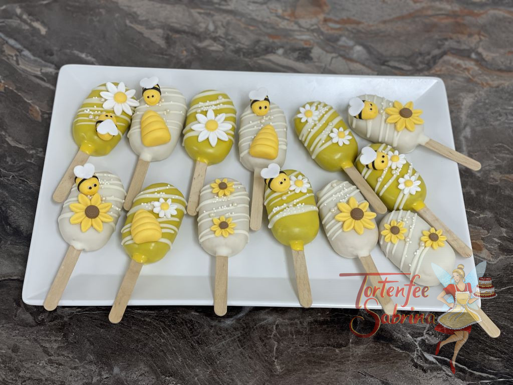 Cakesicles - Bienchen und Blumen zieren die süßen Leckereien, die Schokolade darunter wurde in weiß und gelb gehalten.