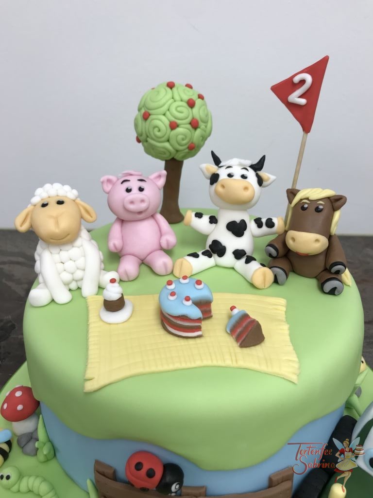 Geburtstagstorte Buben - Bauernhoftiere auf der Wiese, sitzen vergnügt rund um eine Decke mit Leckereien. Ebenfalls auf der Torte ist ein Traktor.