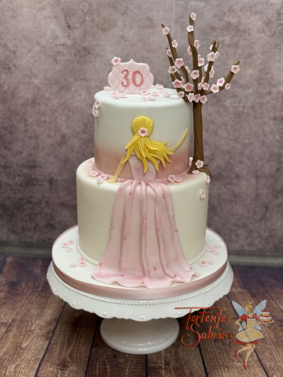 Geburtstagstorte Erwachsene - Blüten im Wind verzieren neben einem Baum und einer Frau im Kleid die zweistöckige Torte.