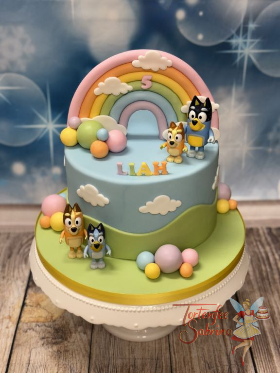 Geburtstagstorte Buben - Bluey und Bingo stehen ganz oben auf der Torte und bewundern den bunten Regenbogen.