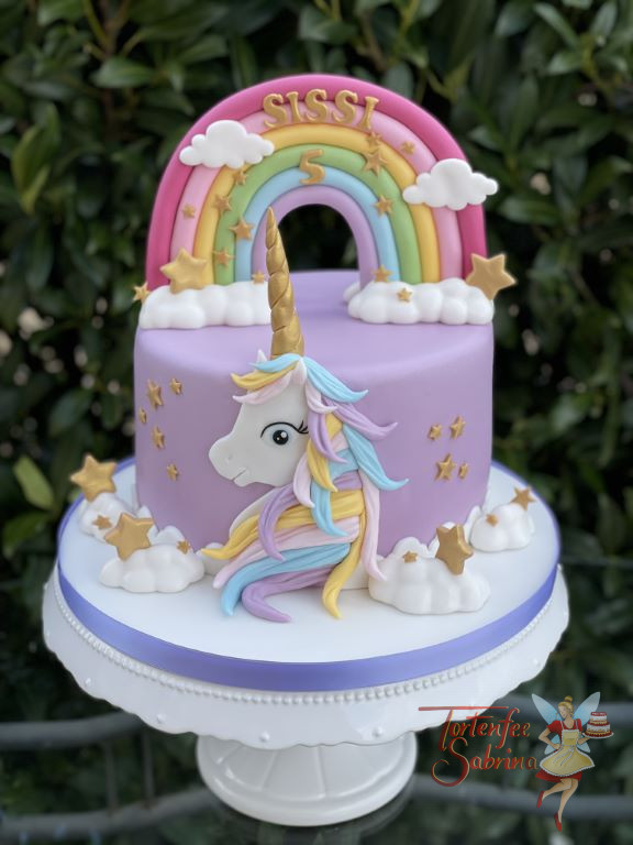 Geburtstagstorte Mädchen - Das zauberhafte Einhorn ist vor der Torte und zeigt ihre bunte Mähne, dahinter der Regenbogen.