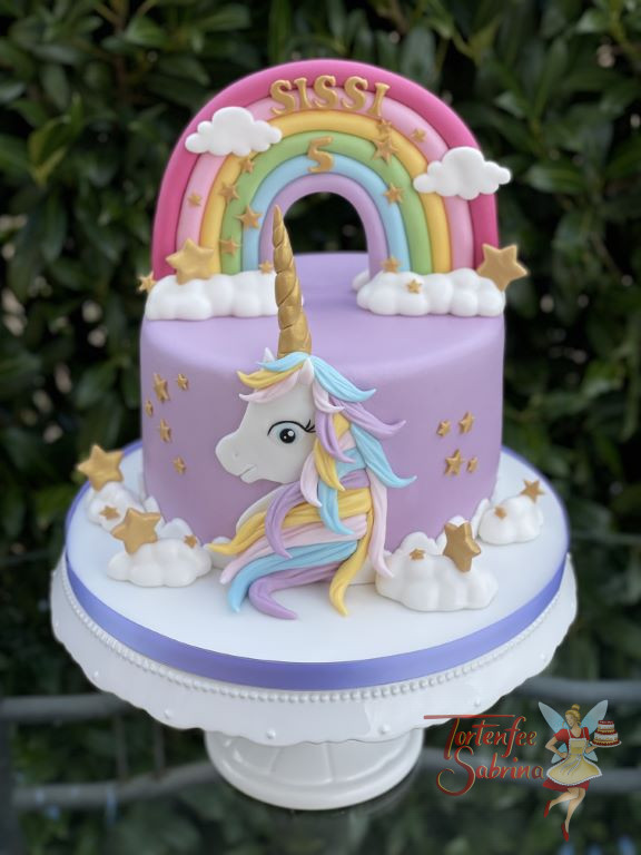 Geburtstagstorte Mädchen - Das zauberhafte Einhorn ist vor der Torte und zeigt ihre bunte Mähne, dahinter der Regenbogen.