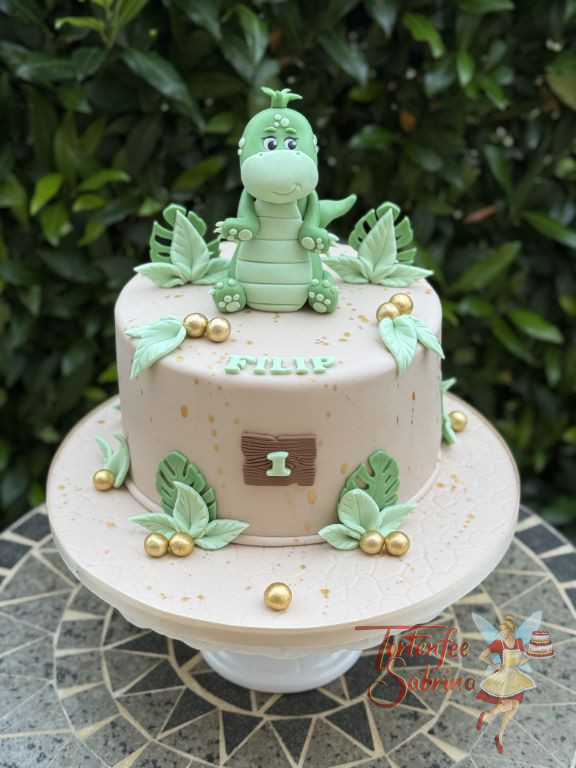 Geburtstagstorte Buben - Der grüne Dino lächelt ganz oben von der Torte herunter, um ihn sind viele grüne Blätter.