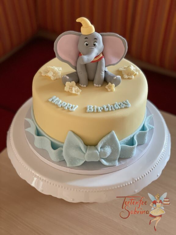 Geburtstagstorte Erwachsene - Dumbo der fliegende Elefant sitzt auf der Torte zwischen Blumen, der untere Abschluß ist eine blaue Schleife.