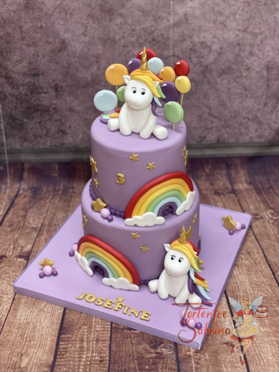 Geburtstagstorte Mädchen - Einhorn mit Luftballons sitzt oben auf der Torte und unten sitzt eines neben dem Regenbogen.