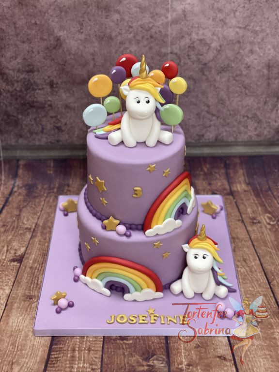 Geburtstagstorte Mädchen - Einhorn mit Luftballons sitzt oben auf der Torte und unten sitzt eines neben dem Regenbogen.