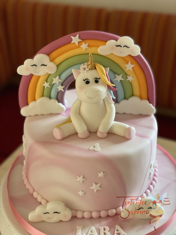 Geburtstagstorte Mädchen - Einhorn mit Wölkchen sitzt vor dem Regenbogen mit Sternchen, die Torte ist rosa und weiß eingedeckt.