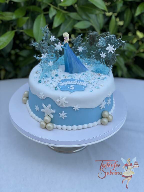 Geburtstagstorte Mädchen - Elsa und die Eiskristalle in mitten der weißen Schneedecke und Schneeflocken mit glitzernden Zuckerperlen.