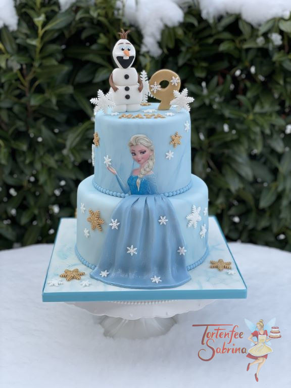 Geburtstagstorte Mädchen - Elsa´s blaues Kleid umgeben von weißen und goldenen Schneeflocken, ganz auf oben auf der Torte ist Olaf.