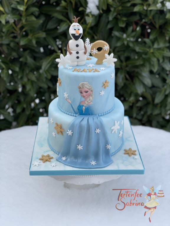 Geburtstagstorte Mädchen - Elsa´s blaues Kleid umgeben von weißen und goldenen Schneeflocken, ganz auf oben auf der Torte ist Olaf.