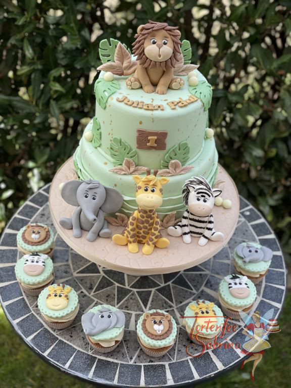 Geburtstagstorte Buben - Fröhliche Dschungeltiere verzieren die zweistöcke Torte und ihre Gesichter sind ebenfalls auf den Cupcakes.