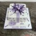 Geburtstagstorte Erwachsene - Geschenkspackerl mit lila und violetter Schleife, ebenso ist die Torte noch mit einer Blume verziert.