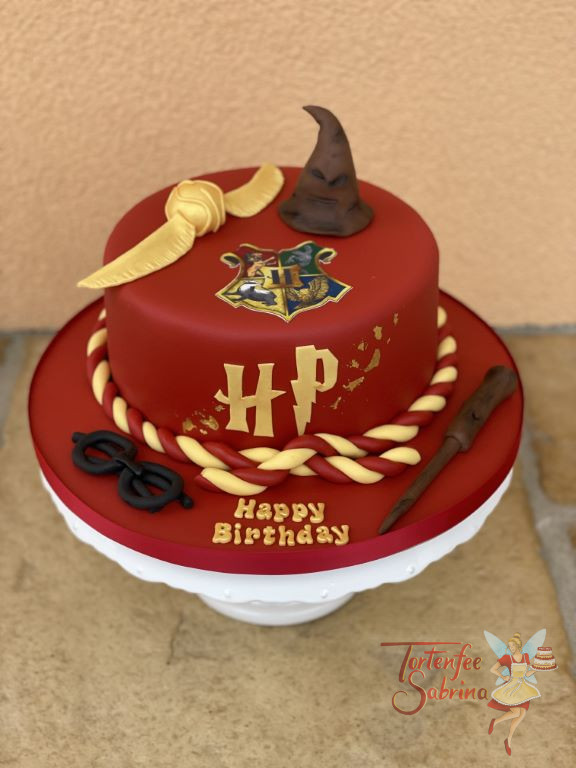 Geburtstagstorte Erwachsene - Hogwarts in Rot, oben auf der Torte ist das Hogwarts-Wappen sowie der sprechende Hut und der goldene Schnatz.