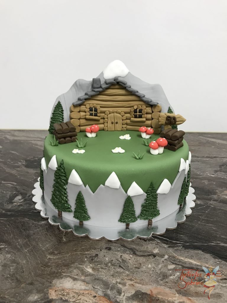 Geburtstagstorte Erwachsene - Hütte in den Bergen. Die Torte stellt eine Wiese mit einer Hütte dar, im Hintergrund ist ein schöner Gipfel.
