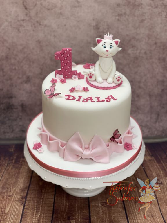 Geburtstagstorte Mädchen - Kätzchen auf der Decke, sitzt und lächelt von der schön verzierten Torte mit rosa Schleife.
