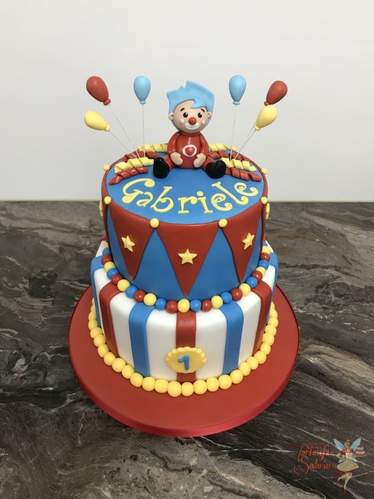 Geburtstagstorte Mädchen - Kleiner roter Clown sitzt auf der Torte die das Muster eines Zirkuszelts hat. Luftballons, Sterne und Lufschlangen sind auch auf der Torte.