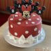 Geburtstagstorte Mädchen - Minnie Mouse mit roter Schleife, sie ziert die rote Torte welche mit weißen Punkten dekoriert ist.