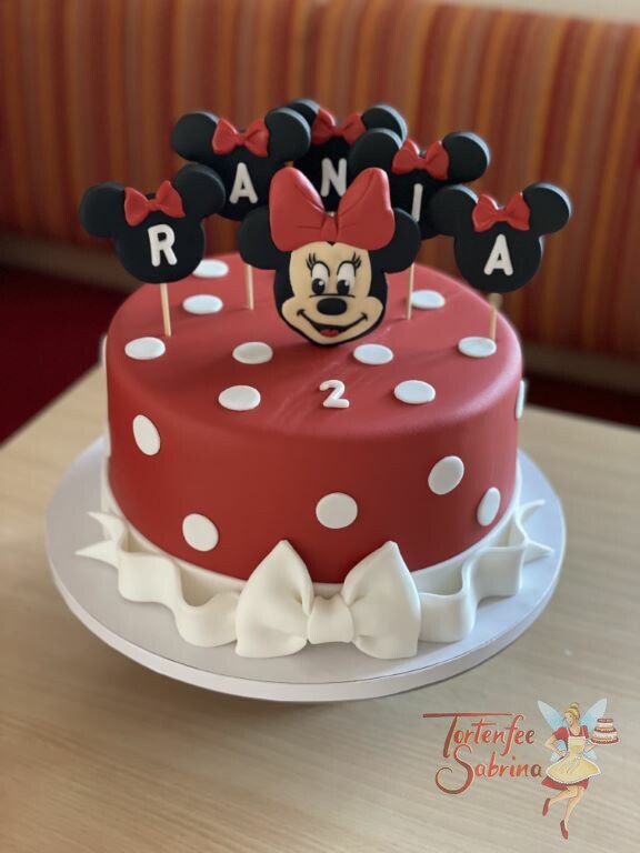 Geburtstagstorte Mädchen - Minnie Mouse mit roter Schleife, sie ziert die rote Torte welche mit weißen Punkten dekoriert ist.