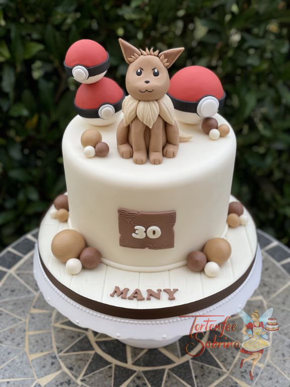 Geburtstagstorte Erwachsene - Niedlicher Evoli sitzt ganz oben auf der Torte und ziert diese neben den rot und weißen Pokebällen.