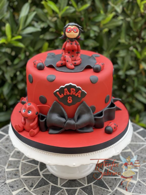 Geburtstagstorte Mädchen - Red Ladybug sitzt oben auf der roten Torte, welche von einer schwarzen Schleife abgeschlossen wird.