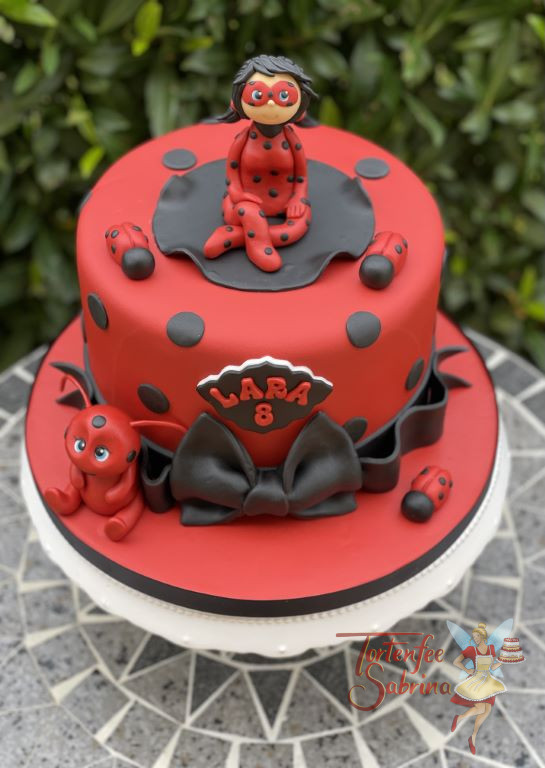 Geburtstagstorte Mädchen - Red Ladybug sitzt oben auf der roten Torte, welche von einer schwarzen Schleife abgeschlossen wird.