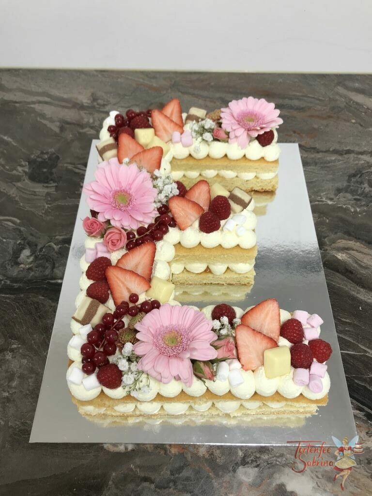 Geburtstagstorte - Süßes blumiges "E" wurde mit rosa Blumen, Erdbeeren, Himbeeren, Ribiselm und verschiedenen Süßigkeiten.
