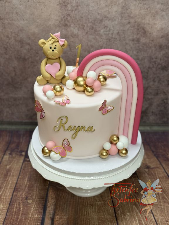 Geburtstagstorte Mädchen - Weiß-Rosa Regenbogen verziert neben den kleinen süßen Teddybären mit Schleife die Torte.