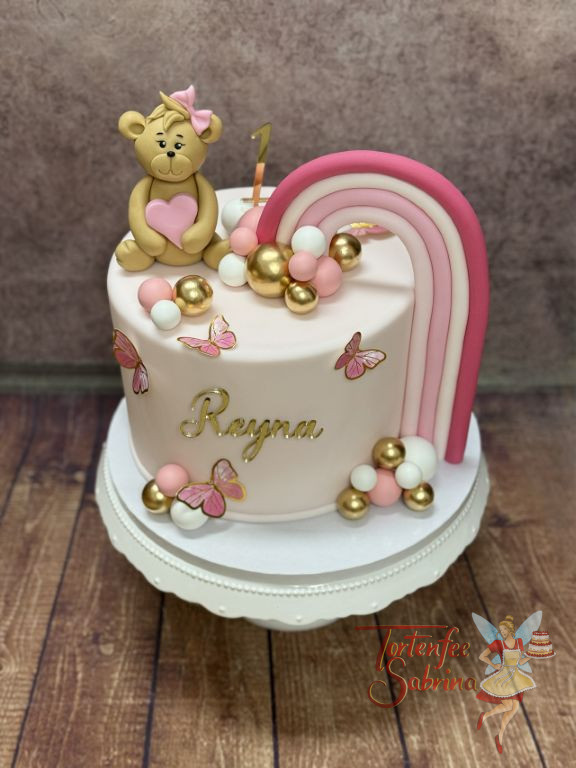 Geburtstagstorte Mädchen - Weiß-Rosa Regenbogen verziert neben den kleinen süßen Teddybären mit Schleife die Torte.