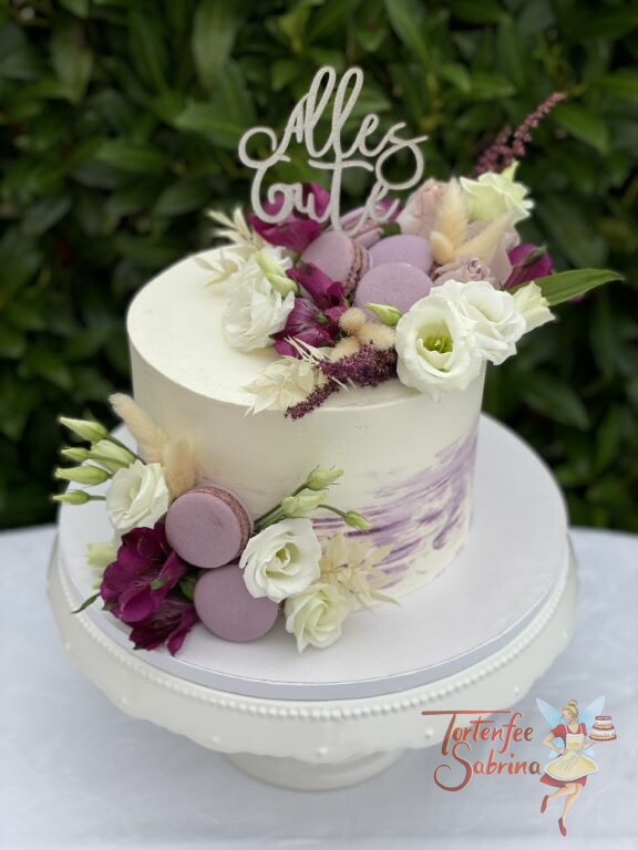 Geburtstagstorte Erwachsene - Weiße und lila Blumen zieren diese schön geschmückte Torte, ebenfalls auf der Torte sind lila Makronen.