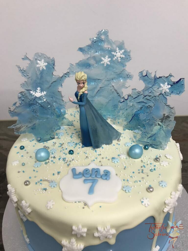 Geburtstagstorte Mädchen - Winterlandschaft der Eiskönigin Elsa. Sie steht zwischen Eisplatten, Kugeln und Schneeflocken.