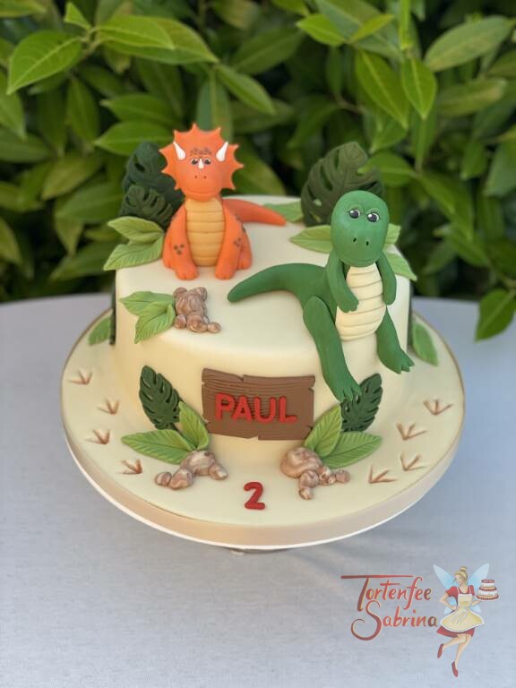 Geburtstagstorte Buben - Zwei Dinos sitzen im Sand und schauen glücklich von der Torte, die auch mit Palmblättern verziert ist.