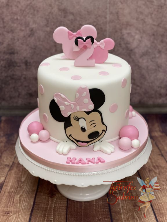 Geburtstagstorte Mädchen - Zwinkernde Minnie Mouse ist ganz vorne auf der Torte und oben verzieren auch noch Schleife die Torte.