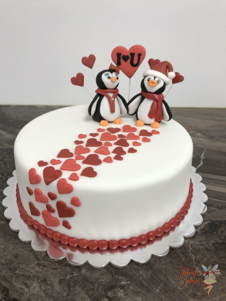 Hochzeitstagstorte - Pinguinspärchen, 2 Pinguine Hand in Hand verziert mit Schal, Haube und Schleife auf einem Weg aus Herzen in rot.