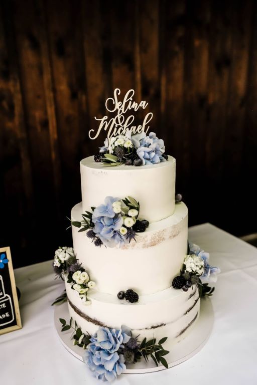 Hochzeitstorte - Blaue Blumen und blaue Beeren verfeinern die Torte und umrahmen unterhalb den personalisierten Caketopper.