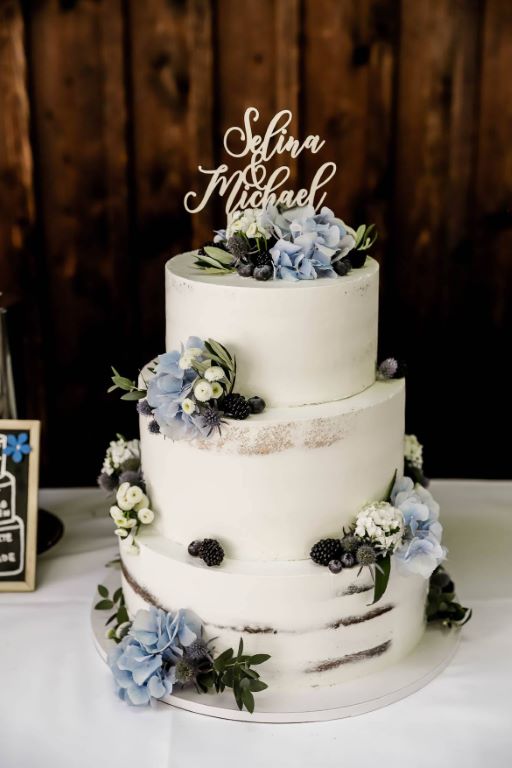 Hochzeitstorte - Blaue Blumen und blaue Beeren verfeinern die Torte und umrahmen unterhalb den personalisierten Caketopper.