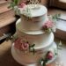 Hochzeitstorte - Blumen mit glänzendem Gold im Bereich der Rosengestecke, ganz oben auf der Torte der passende Topper.