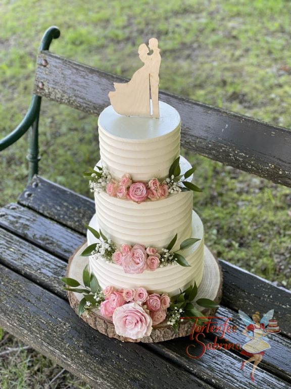 Hochzeitstorte - Das verliebte Brautpaar ist hier als Caketopper auf der mit Rillen und Blumen verzierten dreistöckigen Torte.