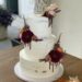 Hochzeitstorte - Dunkelrote Blumen schmücken mit zahlreichen anderen Blumen die Torte, ebenso auf der Torte ist ein Drip aus Schokolade.