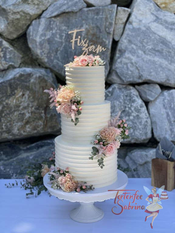 Hochzeitstorte - Feine rosa Blumen und Rillenmuster zieren diese Torte. Hier wurde diese Hochzeitstorte vor einer Steinmauer abgelichtet.