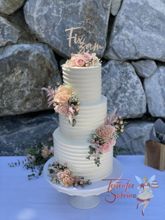 Hochzeitstorte - Feine rosa Blumen und Rillenmuster zieren diese Torte. Hier wurde diese Hochzeitstorte vor einer Steinmauer abgelichtet.