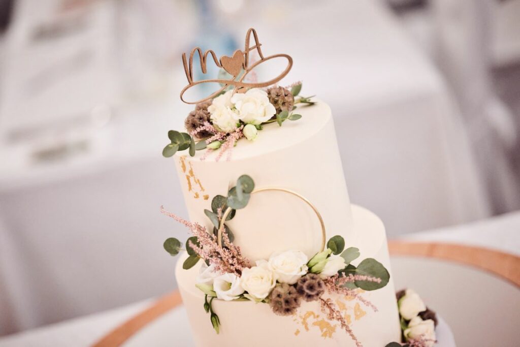 Hochzeitstorte - Goldener Ring mit Blattgold und zarten Blumen mit Blattgrün zieren die zweistöckige weiße Hochzeitstorte.