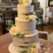 Hochzeitstorte - Große weiße Rosen zieren auf drei Etagen die Hochzeitstorte, die Böden schimmern beim Semi Naked Cake durch.