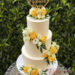 Hochzeitstorte - Herz aus Holz mit den Namen des Brautpaares verziert ganz oben die weiße dreisttöckige Torte neben den Blumenschmuck.