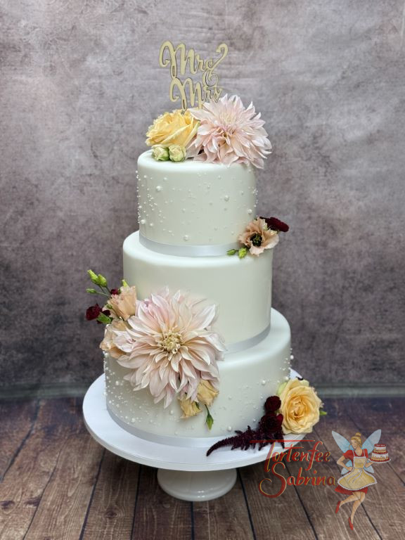 Hochzeitstorte - Kleine weiße Perlen aus Zucker verzieren neben dem weißen Band und den bunten Blüten die dreistöckige Torte.
