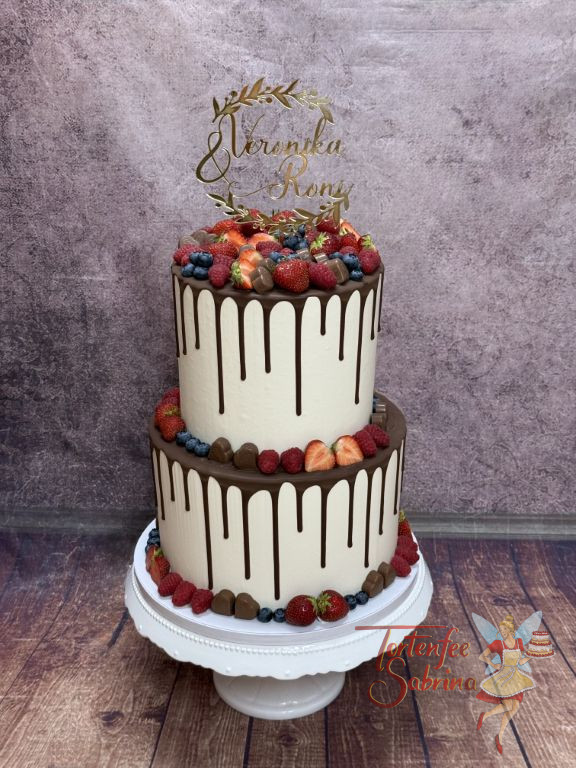 Hochzeitstorte - Köstliche Früchte, wie Erdbeeren und Himbeeren verzieren neben den Schokoherzen den zweistöckigen Drip Cake.