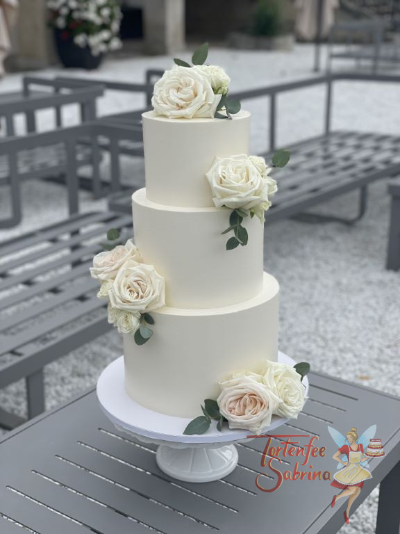 Hochzeitstorte - Prachtvolle weiße Rosen verzieren die dreistöckige Torte, abgerundet wird der Blumenschmuck mit Blattgrün.